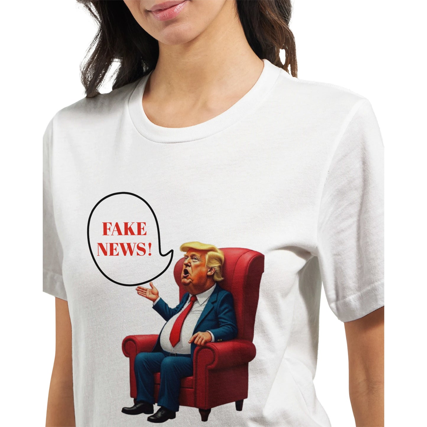 White t-shirt with a colourful cartoon-style caricature of a suited, orange-tinted man sitting in a red armchair, raising one hand and shouting ‘FAKE NEWS!’ in a speech bubble
